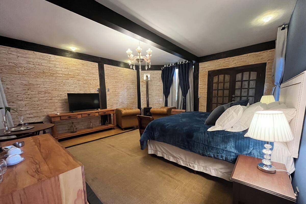 Un dormitorio con una cama grande, televisor, cómoda de madera y candelabro.