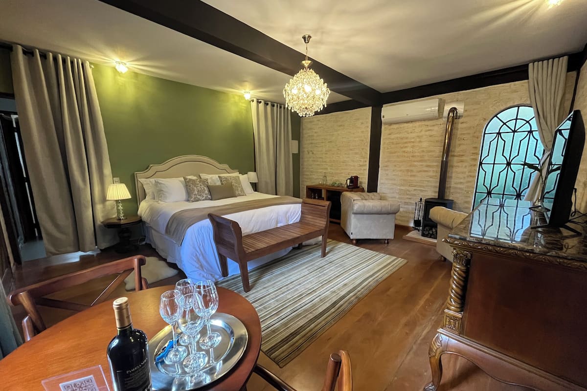 Habitación de hotel con cama, mesita de noche, silla y una mesa de comedor con copas de vino y una botella.