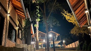 A nighttime view of a building with a stone staircase leading to a wooden deck, surrounded by trees and a well-lit pathway.
