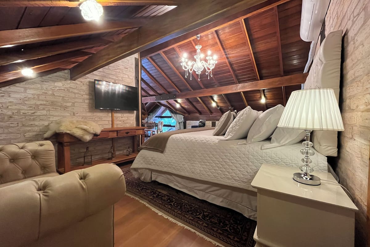 Un dormitorio acogedor en el ático con una cama grande, una araña, un televisor y un sillón de cuero.