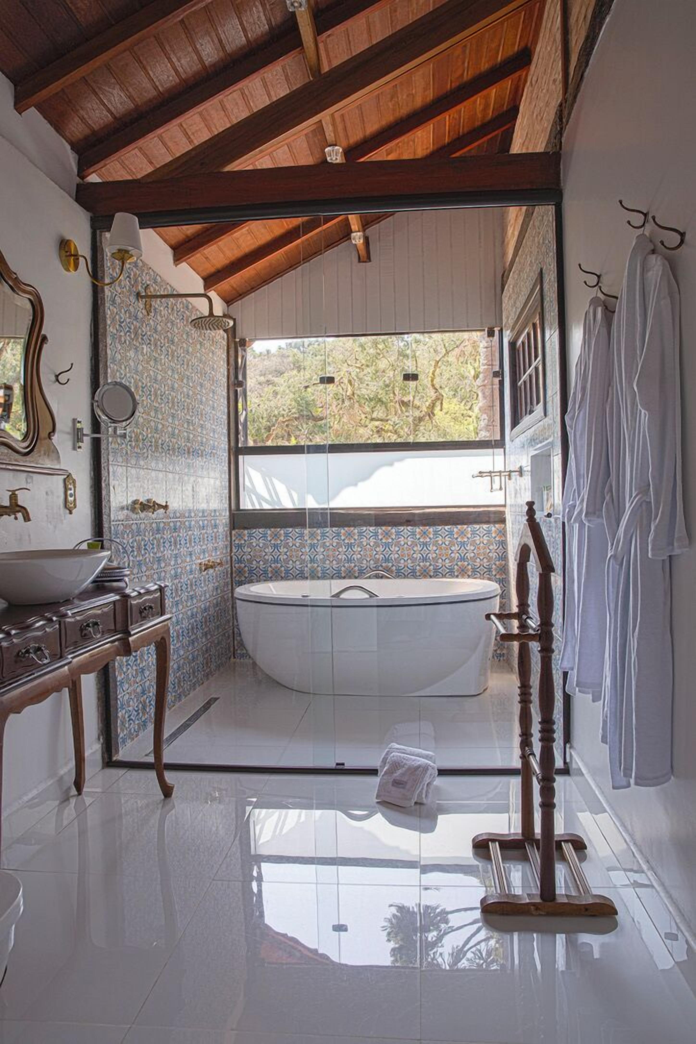 Un baño con una bañera independiente, un tocador con espejo y un ventanal con vistas a zonas verdes.