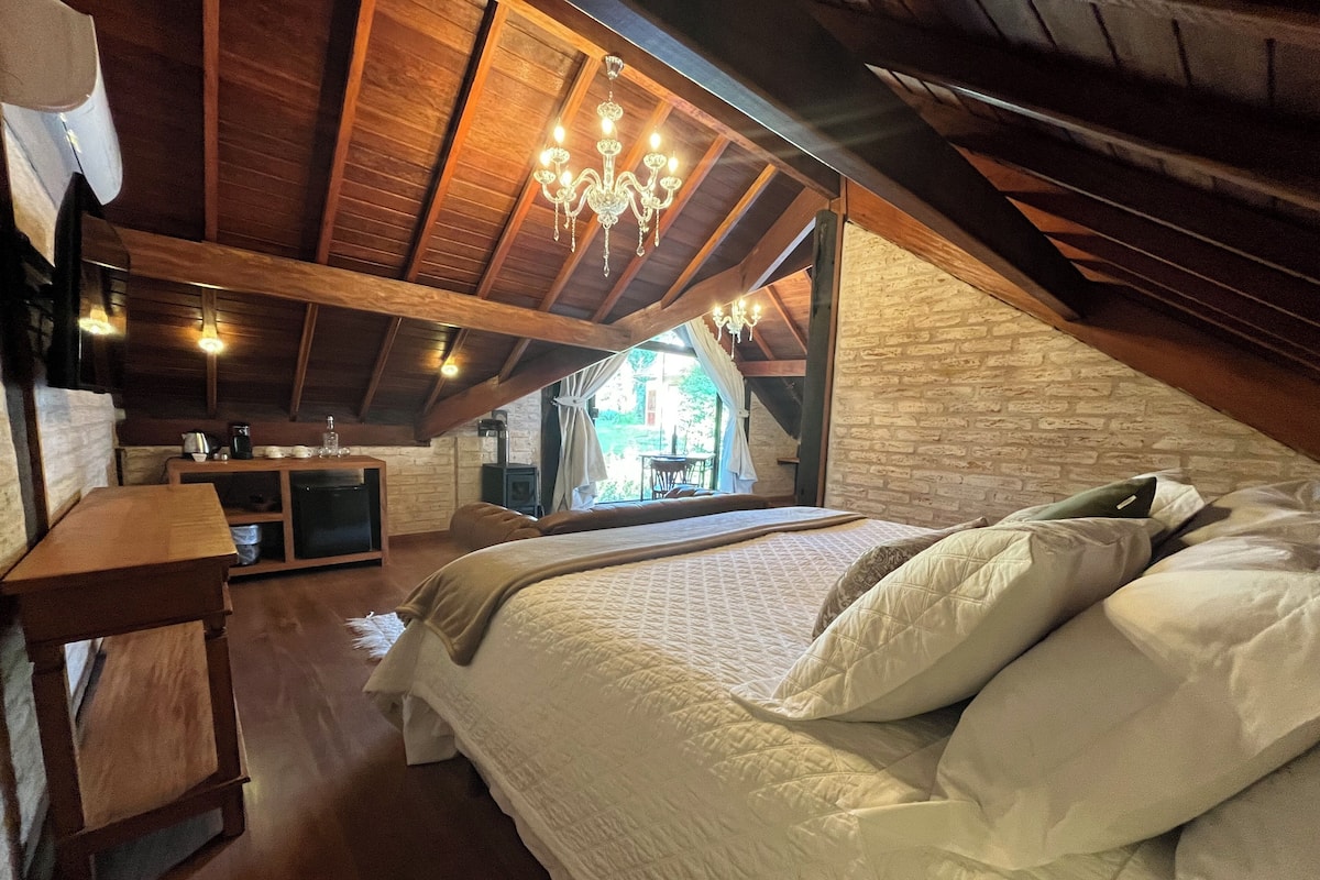 Un dormitorio acogedor en el ático con una cama grande, vigas de madera, una pared de piedra y vistas al exterior.