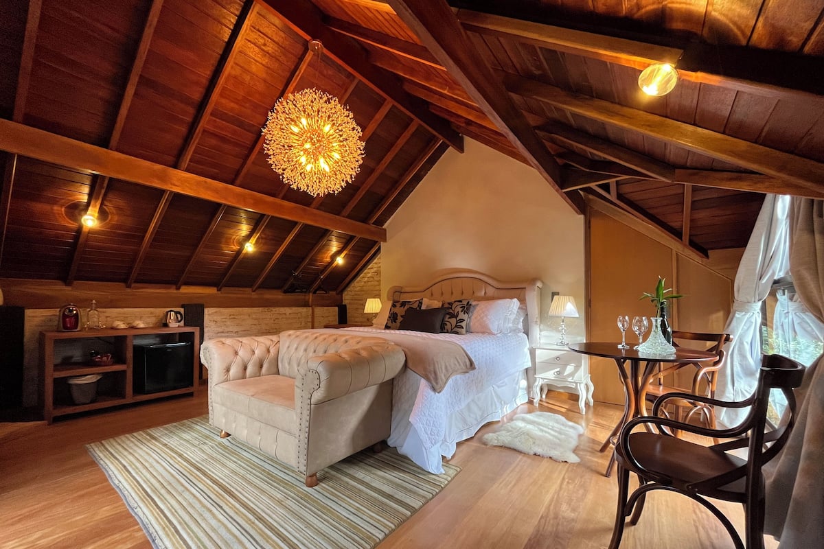 Un dormitorio acogedor con una cama grande, una zona de estar con una mesa y sillas, y un techo de madera.