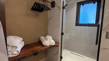 Un baño moderno con mampara de vidrio, repisa de madera con toallas y un ventanal pequeño.