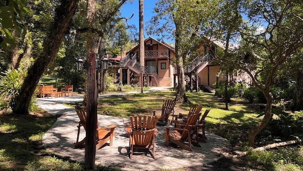 A rustic lodge with a wooden deck, outdoor seating, and a staircase leading to a second-story balcony.