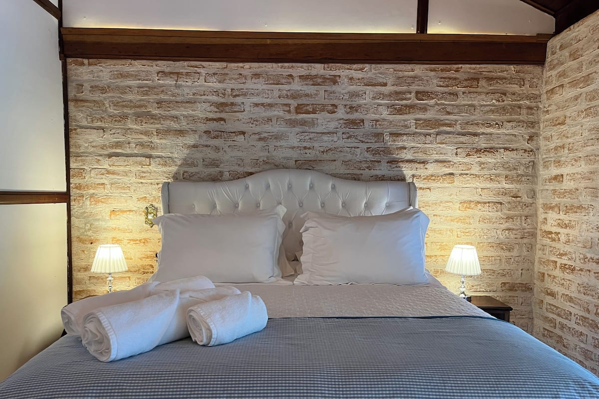 Una cama con cabecera capitonada, dos almohadas y una colcha a cuadros. Hay dos lámparas de noche y una toalla doblada sobre la cama.