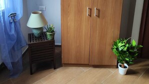 Een kamer met een houten garderobe, een tafeltje met een lamp en potplanten, en een betegelde vloer.