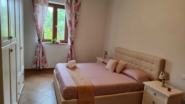 Een slaapkamer met een bed, nachtkastjes, een raam met gordijnen en een kledingkast.