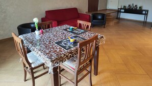 Een eethoek met een tafel voor vier personen, omringd door houten stoelen. Achtergrond toont een rode bank en een zwarte fauteuil.