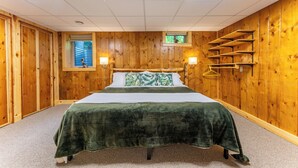 A room with a bed, wooden walls, a window with a view, and a shelf with hangers.