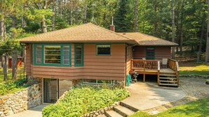 A two-story cabin with a stone foundation, a deck, and a small porch.