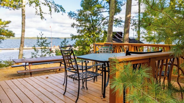A wooden deck with a table and chairs, overlooking a body of water. - A Charming Lakefront Retreat with Resort Comfort (Orr)