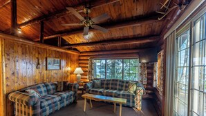 A log cabin interior with a wooden ceiling, two plaid sofas, a wooden coffee table, and large windows. - A Charming Lakefront Retreat with Resort Comfort (Orr)