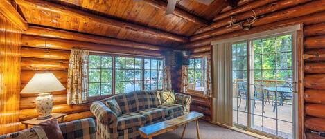 L’intérieur d’une cabane en rondins, avec un canapé à carreaux, une table basse en bois et un ventilateur de plafond.