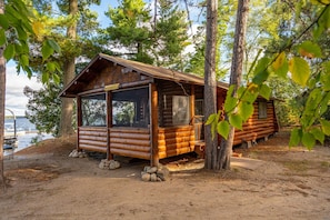A log cabin with a large window, surrounded by trees and a body of water.