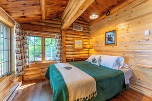 A log cabin bedroom with a bed, a map, a lamp, and a window with curtains.