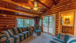 A log cabin interior with a striped sofa, a chair, a ceiling fan, and a large window. - Spacious Comfort with a Private Dock (Orr)