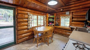 A log cabin interior with a wooden dining table, chairs, a kitchen area with a sink, and a window overlooking a wooded area. - Spacious Comfort with a Private Dock (Orr)