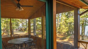 A covered outdoor seating area with a table and chairs, overlooking a wooded area and a body of water. - Vaulted Ceilings and a Stunning Main Room (Pet-Friendly) (Orr)