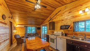 A cozy cabin interior with a wooden dining table, a sofa, a kitchen with a stove, microwave, and sink. - Vaulted Ceilings and a Stunning Main Room (Pet-Friendly) (Orr)