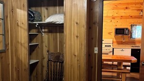 A room with a bunk bed, a wooden wardrobe, a chair, a bed with a floral bedspread, a wooden table, and a kitchenette with a microwave and sink. - Vaulted Ceilings and a Stunning Main Room (Pet-Friendly) (Orr)