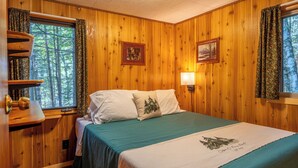 A wooden-paneled room with a bed, two windows with curtains, a wall-mounted lamp, and a framed picture. - The Most Private, Pet-Friendly Cabin (New Screened Porch in 2024) (Orr)