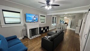 Un salón espacioso con chimenea, ventilador de techo y un televisor grande montado en la pared.