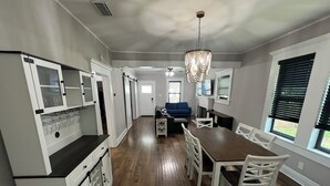 Una cocina amplia con piso de madera, muebles de cocina blancos y un comedor con mesa de madera y sillas blancas.