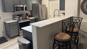 Una cocina moderna con gabinetes grises, electrodomésticos de acero inoxidable, una encimera de mármol y una pequeña zona de bar con taburetes.