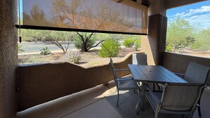 Un patio techado con mesa y sillas, un ventilador de techo y vistas a un estacionamiento y árboles.