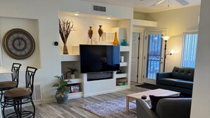 Una sala de estar moderna con televisor de pantalla plana, piso de madera, ventilador de techo y comedor con sillas.