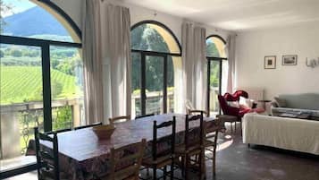 A dining area with a table and chairs, large arched windows with curtains, a red chair, and a white sofa.