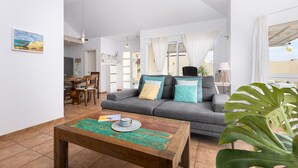 A spacious living room with a grey sofa, a wooden coffee table, and a dining area in the background.