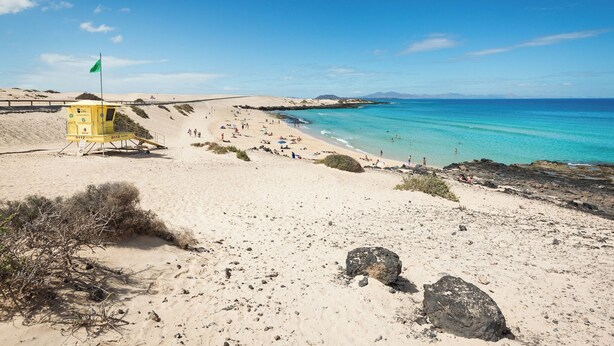 A sandy beach with a lifeguard tower and clear blue waters.