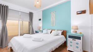 A bedroom with a bed, a nightstand, a macrame wall hanging, and a view through a sliding door.