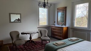 A bedroom with a bed, two chairs, a table, a dresser, a mirror, and a chandelier. - Villa Marani monte matello (TEOLO)
