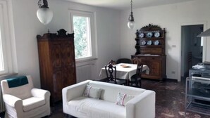 A room with a white sofa, a wooden cabinet, and a dining table with chairs. - Villa Marani monte matello (TEOLO)