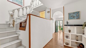 Una escalera con escalones blancos y barandillas de madera, que lleva a una plataforma con una consola blanca y estanterías.