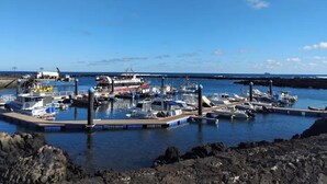 Un puerto deportivo con varias embarcaciones amarradas, un muelle y un litoral rocoso.