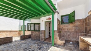 Un espacio al aire libre cubierto con suelo de piedra, ventanas de marco verde y un banco.