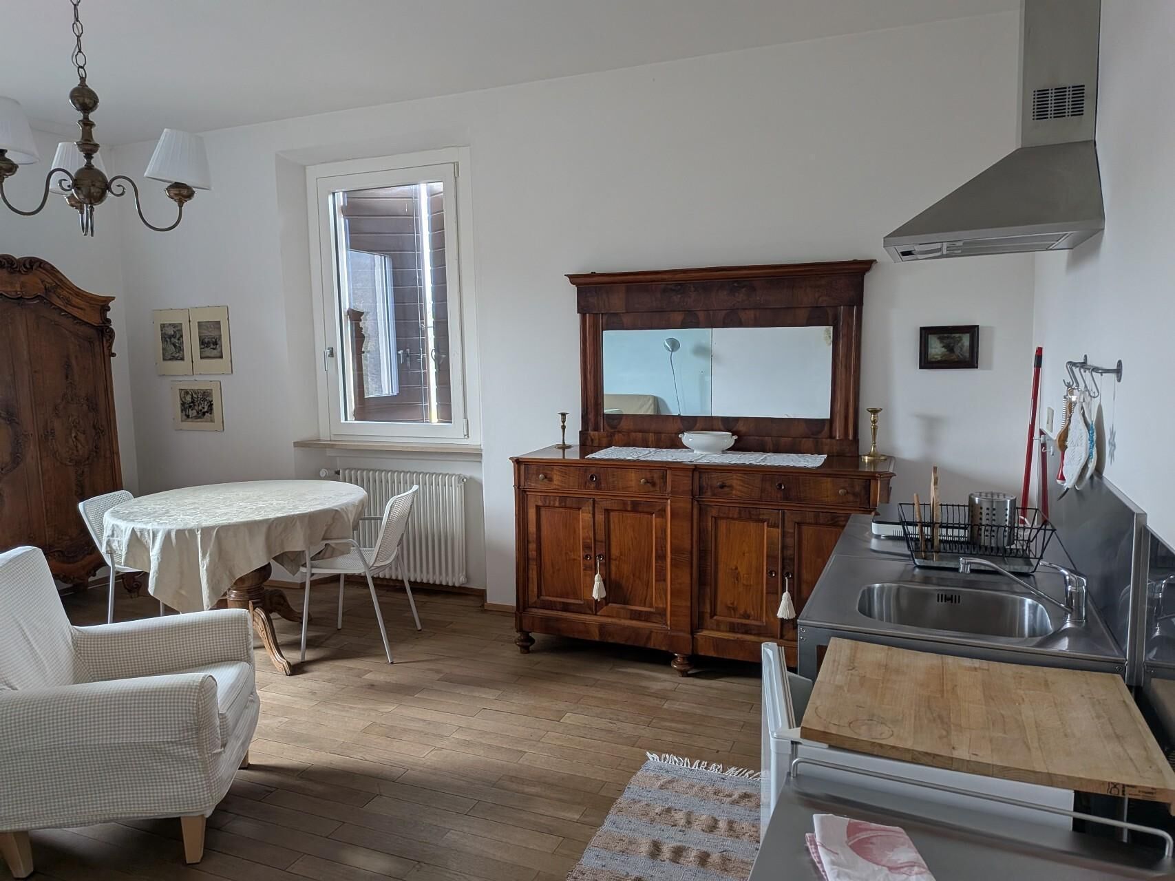 Une cuisine avec un meuble en bois, une table à manger, une chaise, un radiateur et une fenêtre.