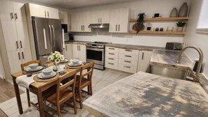 Una cocina moderna con armarios blancos, electrodomésticos de acero inoxidable y un comedor con mesa y sillas de madera.