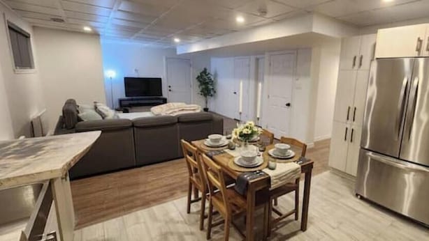 Una cocina moderna con una mesa de comedor para cuatro personas, un refrigerador de acero inoxidable grande y una zona de estar acogedora con un sofá y televisor.