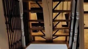 Una escalera que sube a un rellano en el segundo piso, con una puerta en la parte inferior.