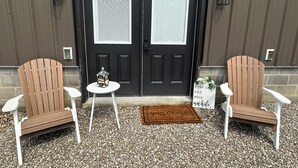A black double door with a welcome mat in front, two wooden chairs, and a small table with a decorative item.