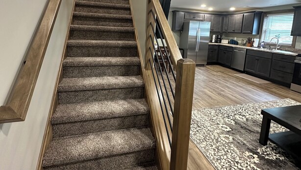 A staircase leading to a kitchen with dark wooden cabinets and a stainless steel refrigerator.