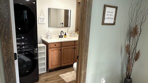 A modern bathroom with a large mirror, wooden cabinets, a sink, and a black washing machine.