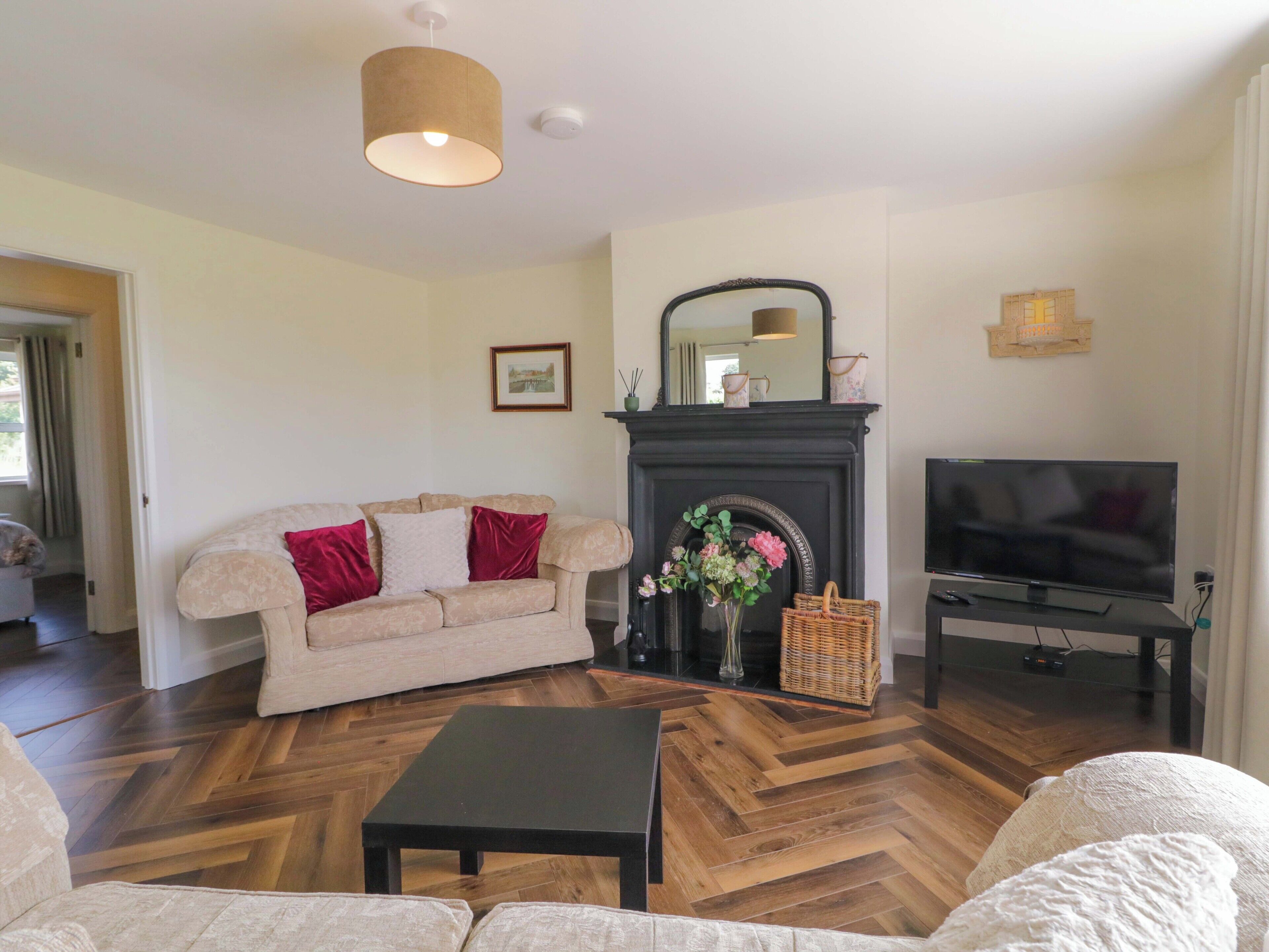 A living room with a sofa, a coffee table, a fireplace, a television, and a herringbone-patterned floor.