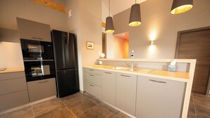 A modern kitchen with a black refrigerator, stainless steel appliances, and a wooden ceiling.