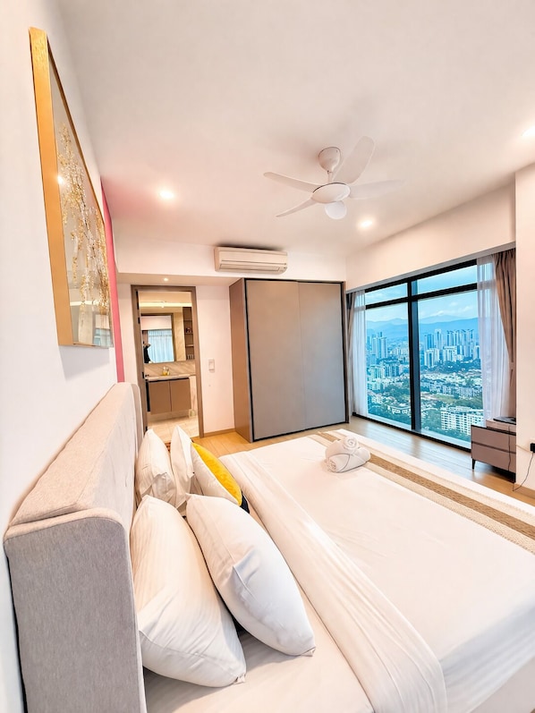 A modern hotel room with a large bed, a ceiling fan, an air conditioning unit, a view of a cityscape through large windows, and a small desk with a chair. - Eaton Residence by crystal (Kuala Lumpur)